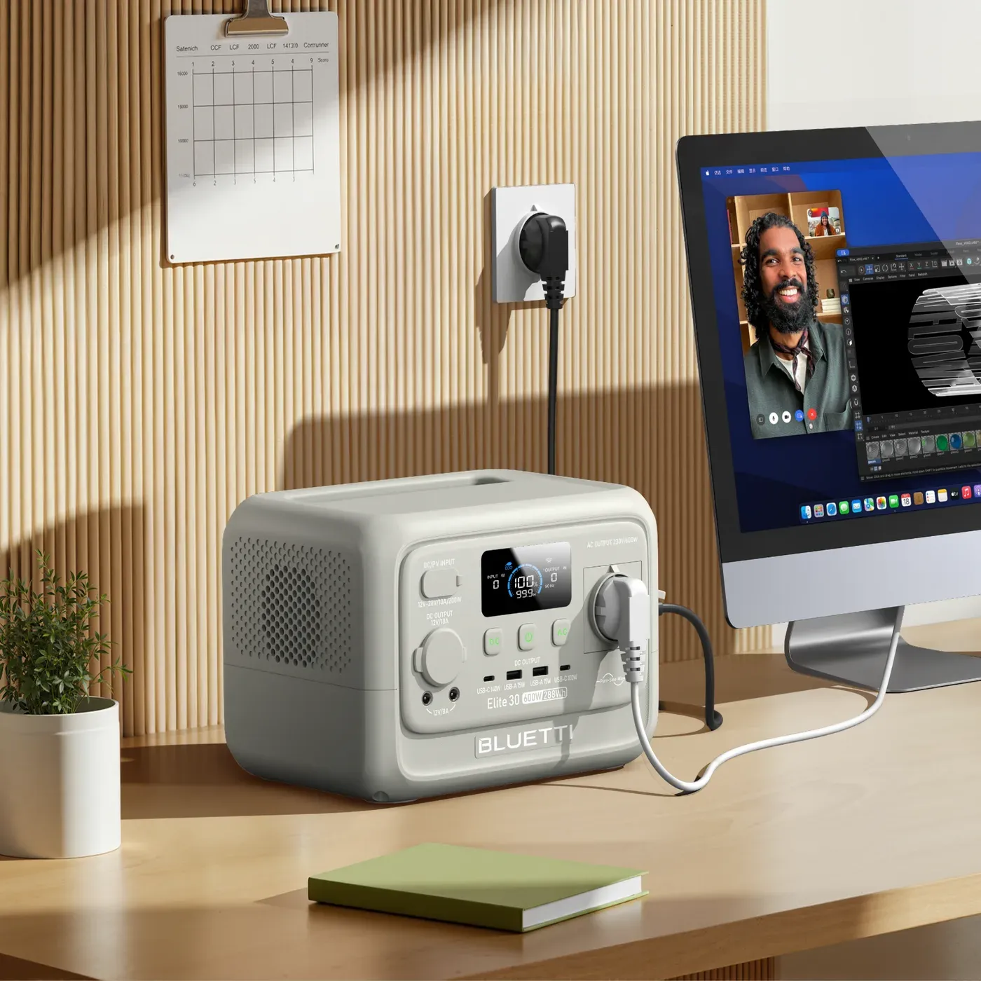 L'Elite 30 V2 posée sur un bureau, intercalée entre la prise murale et un ordinateur de bureau allumé